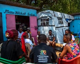 A community dialogue circle outside brightly painted market kiosks.